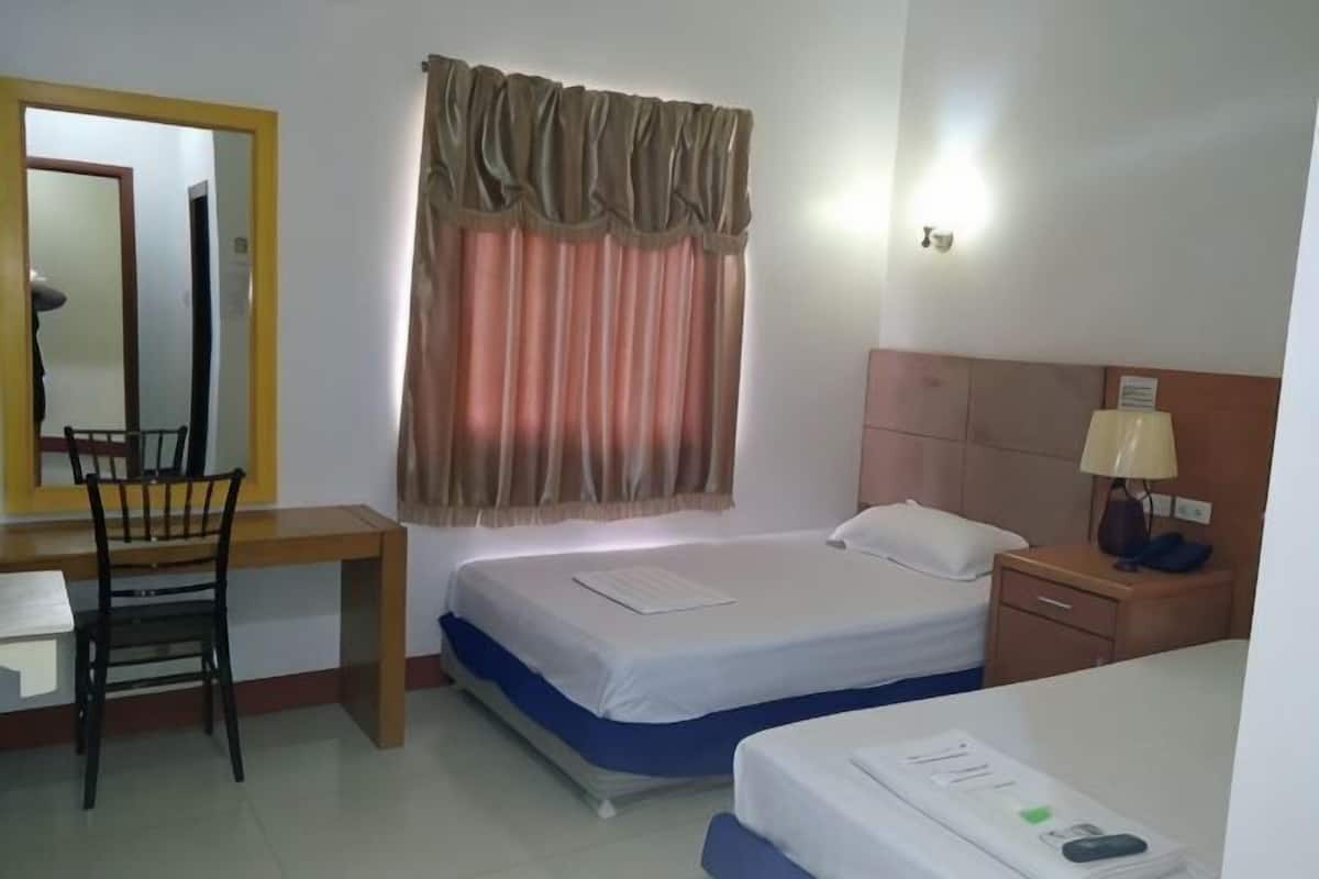 A hotel room with a bed, a desk, a chair, a nightstand with a lamp, and a window with curtains.