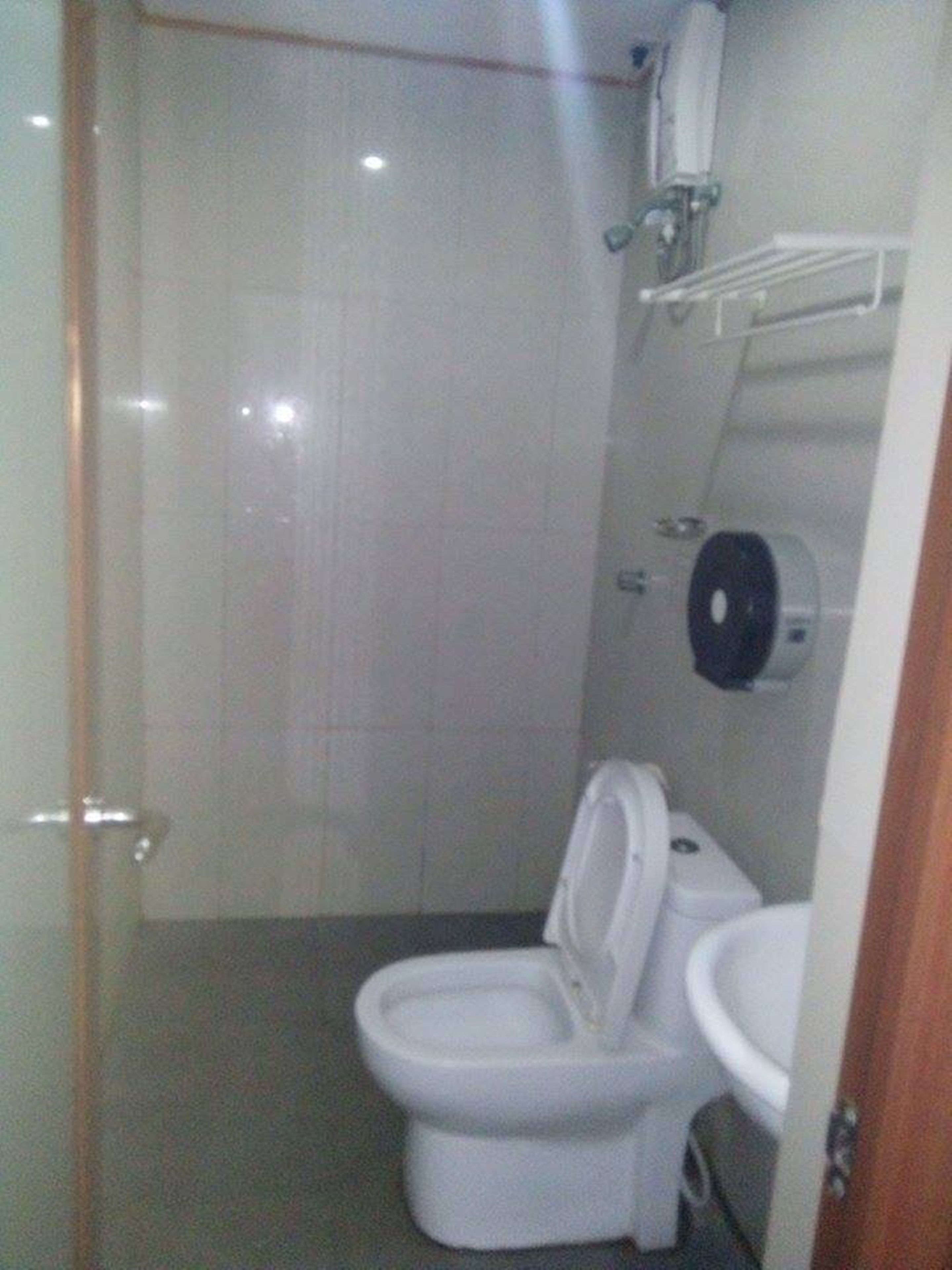 A small, compact bathroom with a toilet and sink, a towel dispenser, and a toilet paper holder on the wall.