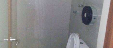 A small, compact bathroom with a toilet and sink, a towel dispenser, and a toilet paper holder on the wall.