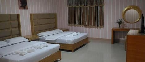 A hotel room with two wooden beds, a wooden dresser, a round mirror, and a window with curtains.