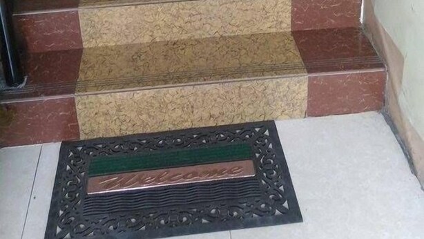 Eine Treppe mit abwechselnd dunklen und hellen Marmorstufen, einem Geländer und einer Fußmatte mit dem Aufdruck 'Welcome' am unteren Ende.