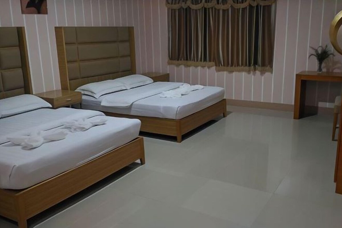 A hotel room with two beds, a wooden headboard, a bedside table, a mirror, and a window with curtains.