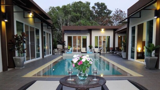 A pool area with a glass table and chairs, surrounded by modern buildings with large windows. - Residence Harmonie (Rawai)
