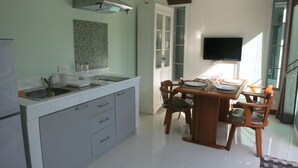 A modern kitchen with a dining area, a built-in oven, and a flat-screen TV mounted on the wall. - Residence Harmonie (Rawai)