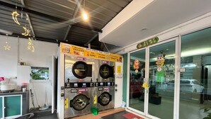 A commercial laundry facility with two dryers and two washing machines, a tiled floor, and a glass door entrance. - The Garden Inn (Miri)