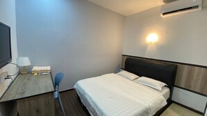 A compact hotel room with a bed, a desk with a lamp, a chair, and a wall-mounted air conditioner. - The Garden Inn (Miri)