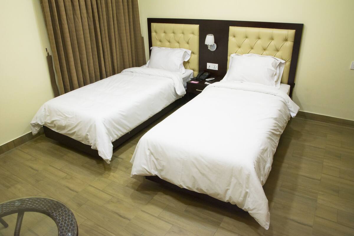 A hotel room with two single beds, a wooden floor, and a chair.