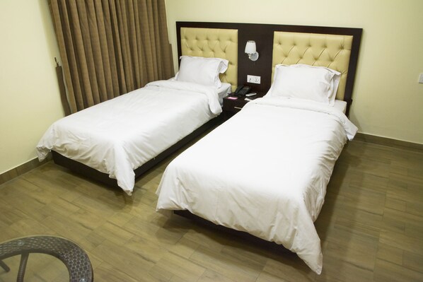 A hotel room with two single beds, a wooden floor, and a chair.