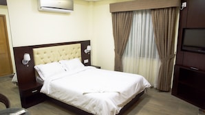 A hotel room with a large bed, a television, a bedside table with a lamp, and a window with curtains. - Nandan Village Resort (Chandra)