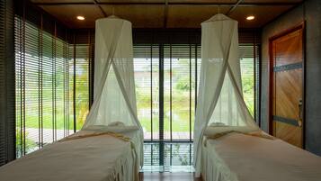 Una habitación con dos camas, cada una con dosel, ventanas amplias con persianas y una puerta de madera.