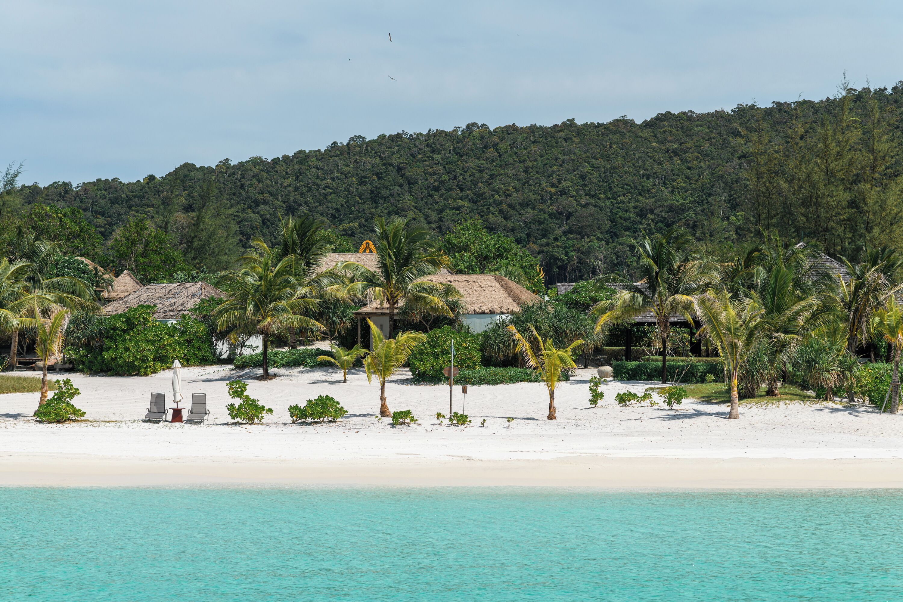 A beach resort with thatched-roof huts, palm trees, and a white sandy beach.