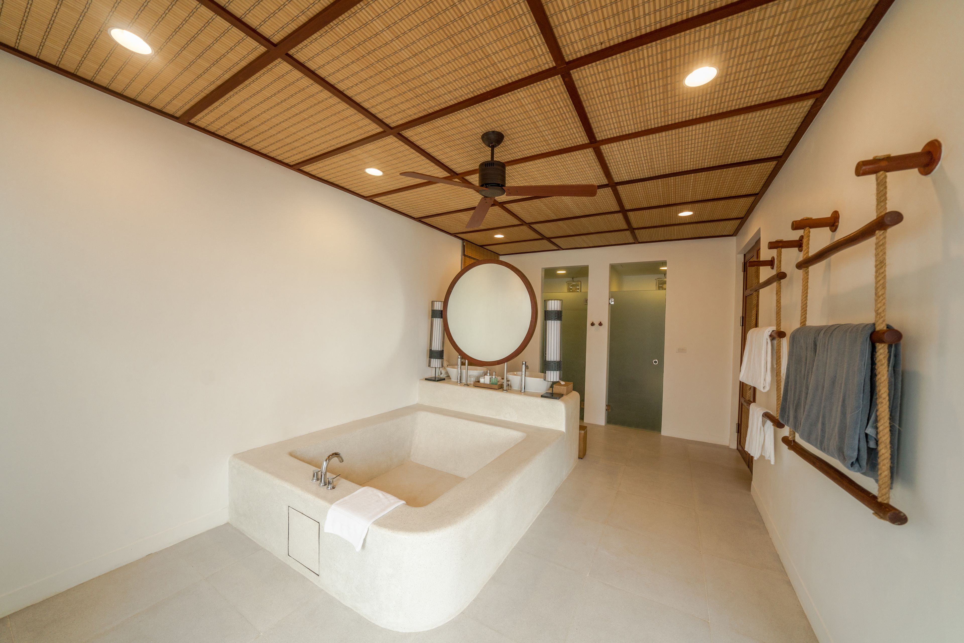 A modern bathroom with a freestanding bathtub, a ceiling fan, and a towel rack with towels.