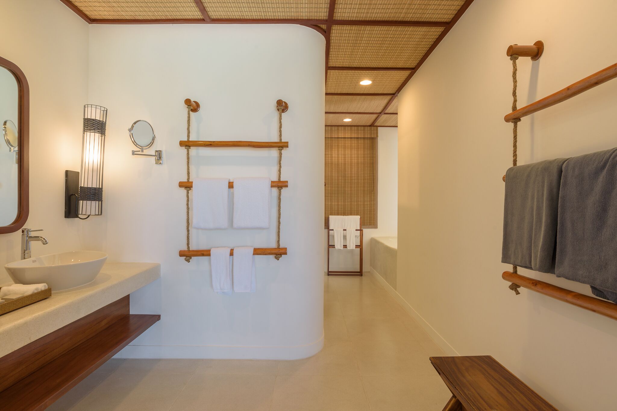 A modern bathroom with a large sink, wooden towel racks, a mirror, and a wooden bench.