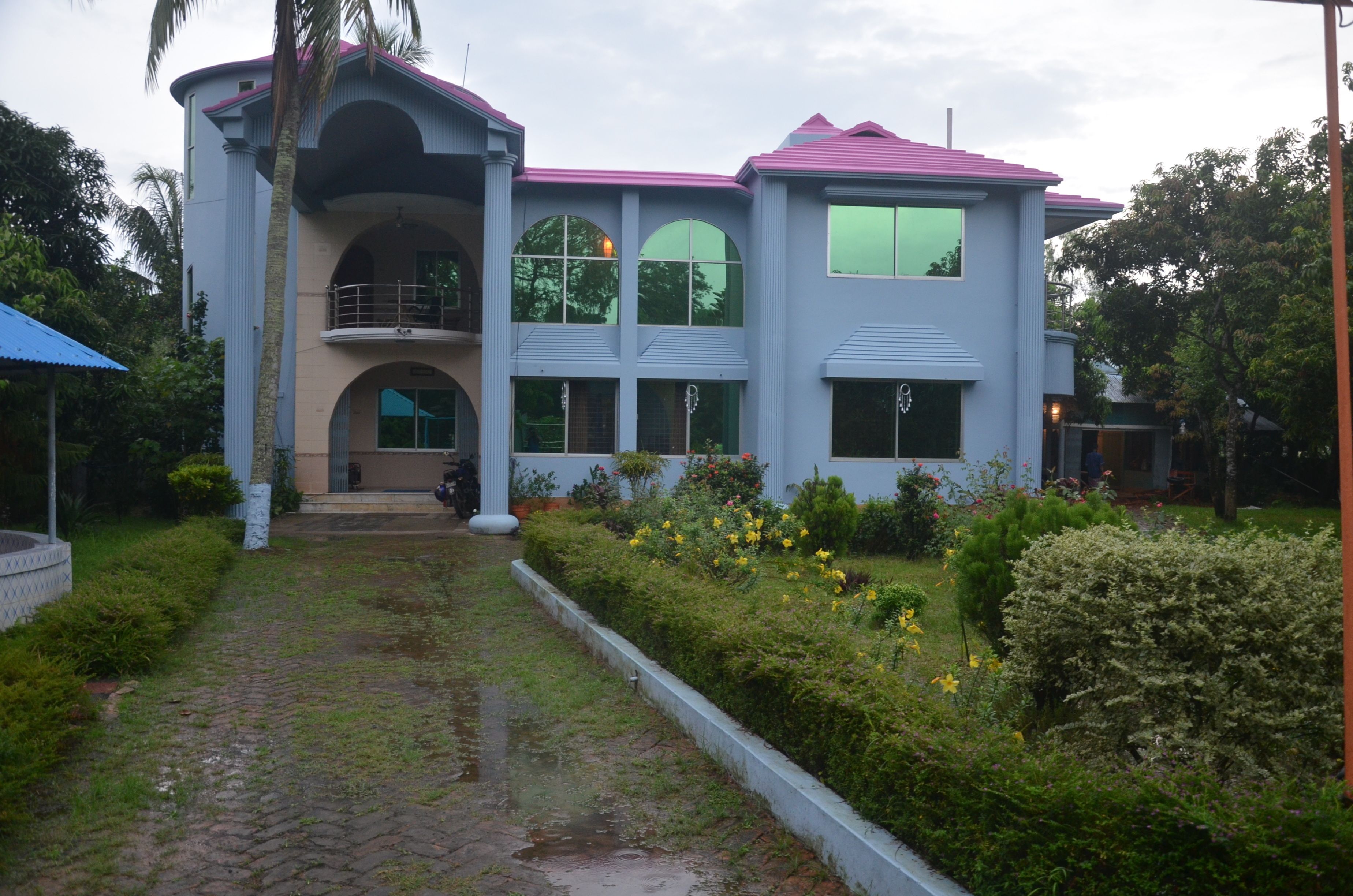 A two-story building with a balcony, large windows, and a garden with flowers.