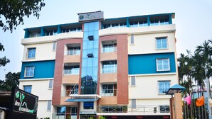 A multi-story hotel with a central glass elevator shaft, multiple balconies, and a parking area. - Tea Heaven Resort (Sreemangal)