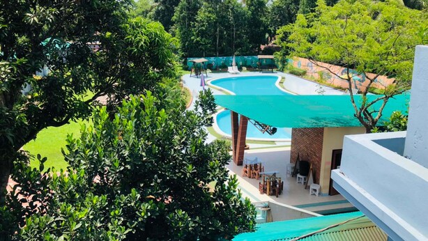 A resort with a large swimming pool surrounded by lush greenery and a covered outdoor seating area. - Tea Heaven Resort (Sreemangal)