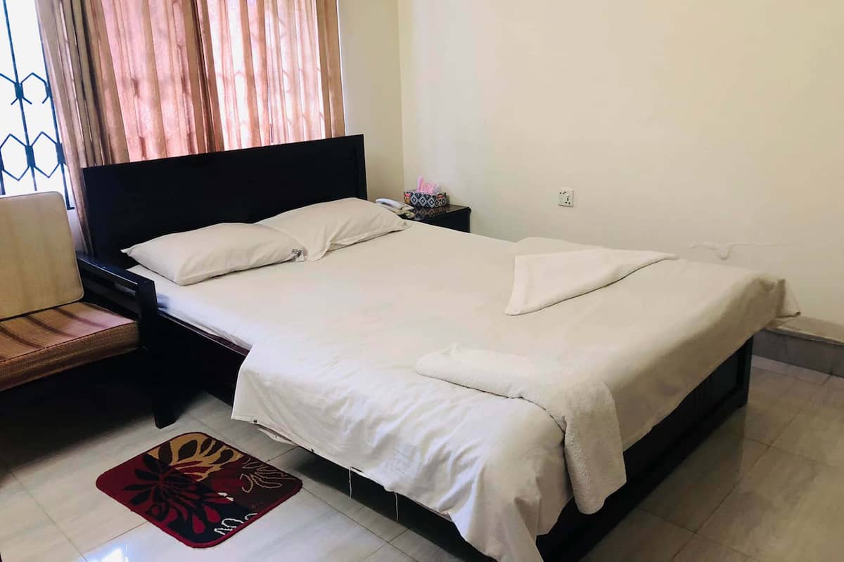 A neatly made bed with white linens, a wooden headboard, and a bedside table with a phone and decorative items.