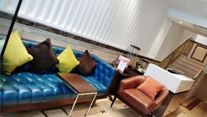 Uma sala de estar moderna com um sofá azul, poltrona de couro marrom e uma pequena mesa lateral de madeira.