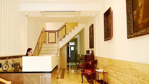 Um saguão de hotel com balcão de recepção, escada e parede decorada com obras emolduradas.