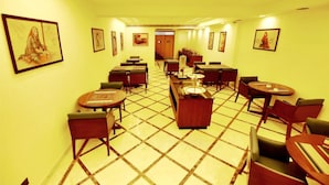 Um corredor de hotel com várias mesas e cadeiras para refeições, piso ladrilhado e quadros nas paredes.