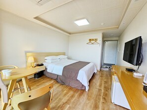A hotel room with a bed, a desk with a lamp, a television, and a kitchenette. - Hotel Lavender Jeju (Seogwipo)