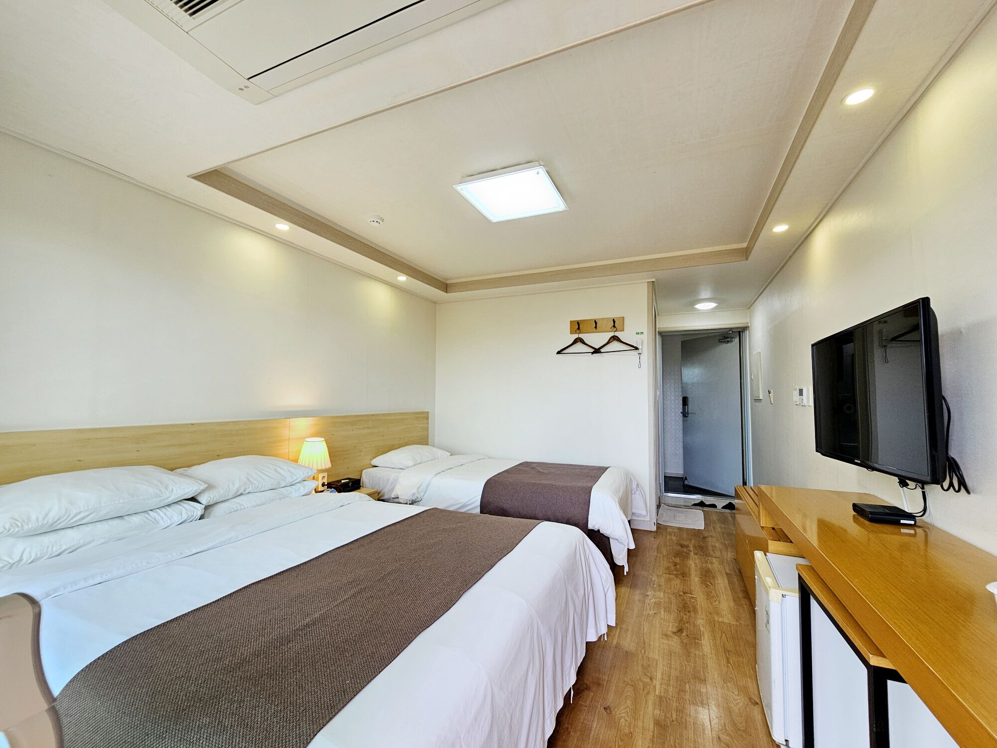 A hotel room with three beds, a TV, a desk, and a walk-in closet.