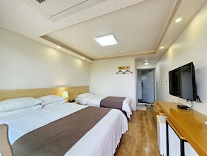 Quarto de hotel com três camas, televisão, escrivaninha e closet espaçoso.