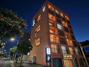 Um hotel com vários andares, um letreiro grande com a letra 'N', varandas e um letreiro 'P' para estacionamento.