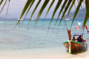 A boat docked at a beach with clear turquoise water and a mountainous backdrop.