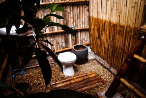 A bamboo-walled bathroom with a toilet, a large pot, and a plant.