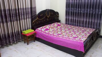 A bedroom with a bed, curtains, a small stool, and a tiled floor.