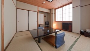 A traditional Japanese-style room with tatami flooring, a low table with cushions, a television, and a large window providing natural light. - Subaruyado Yoshino (Tokushima)