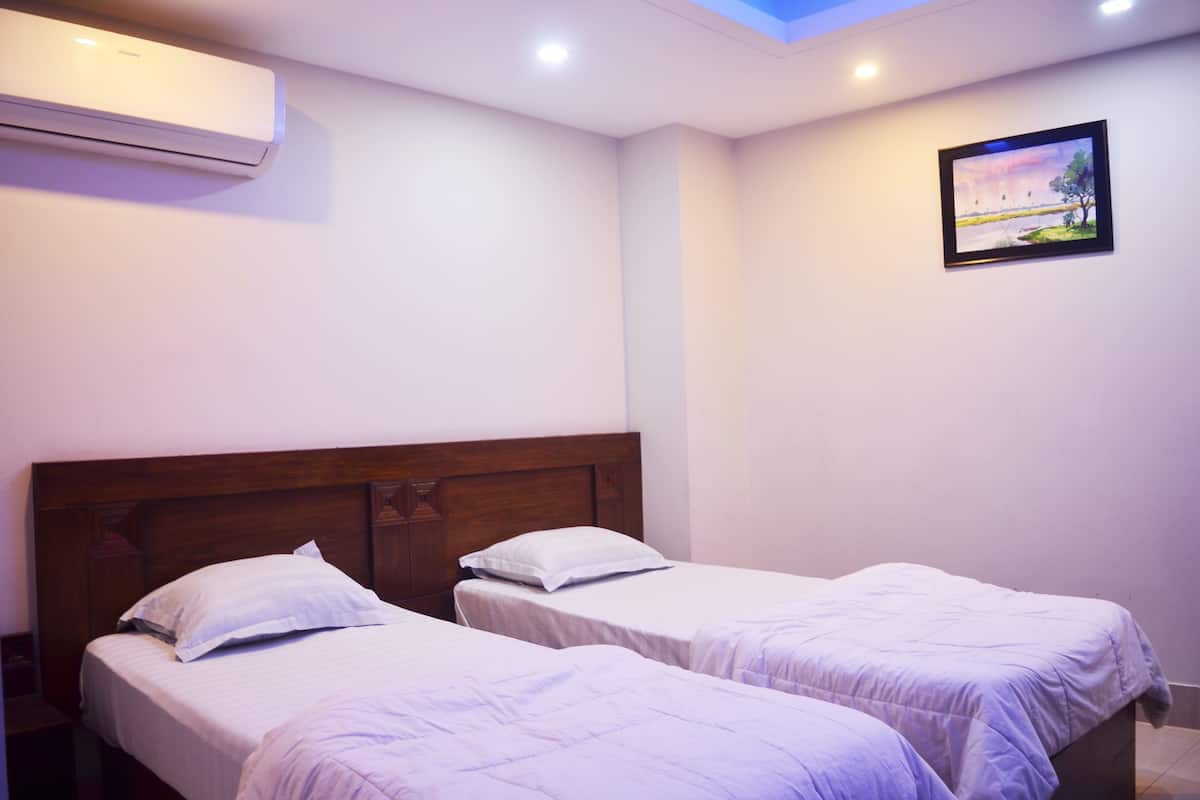 A room with two single beds, a wooden headboard, an air conditioning unit, and a framed landscape picture on the wall.