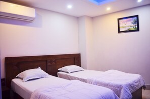 A room with two single beds, a wooden headboard, an air conditioning unit, and a framed landscape picture on the wall.