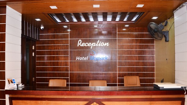 Un comptoir d’accueil avec un revêtement en bois, une enseigne indiquant « Réception, hôtel Skypark », et deux chaises.