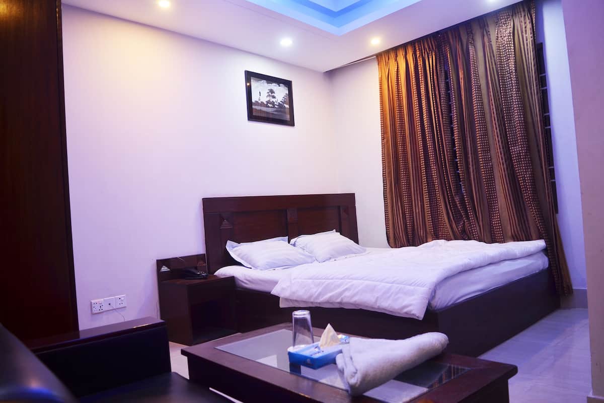 A hotel room with a large bed, a bedside table, a nightstand, a mirror, and a ceiling light.