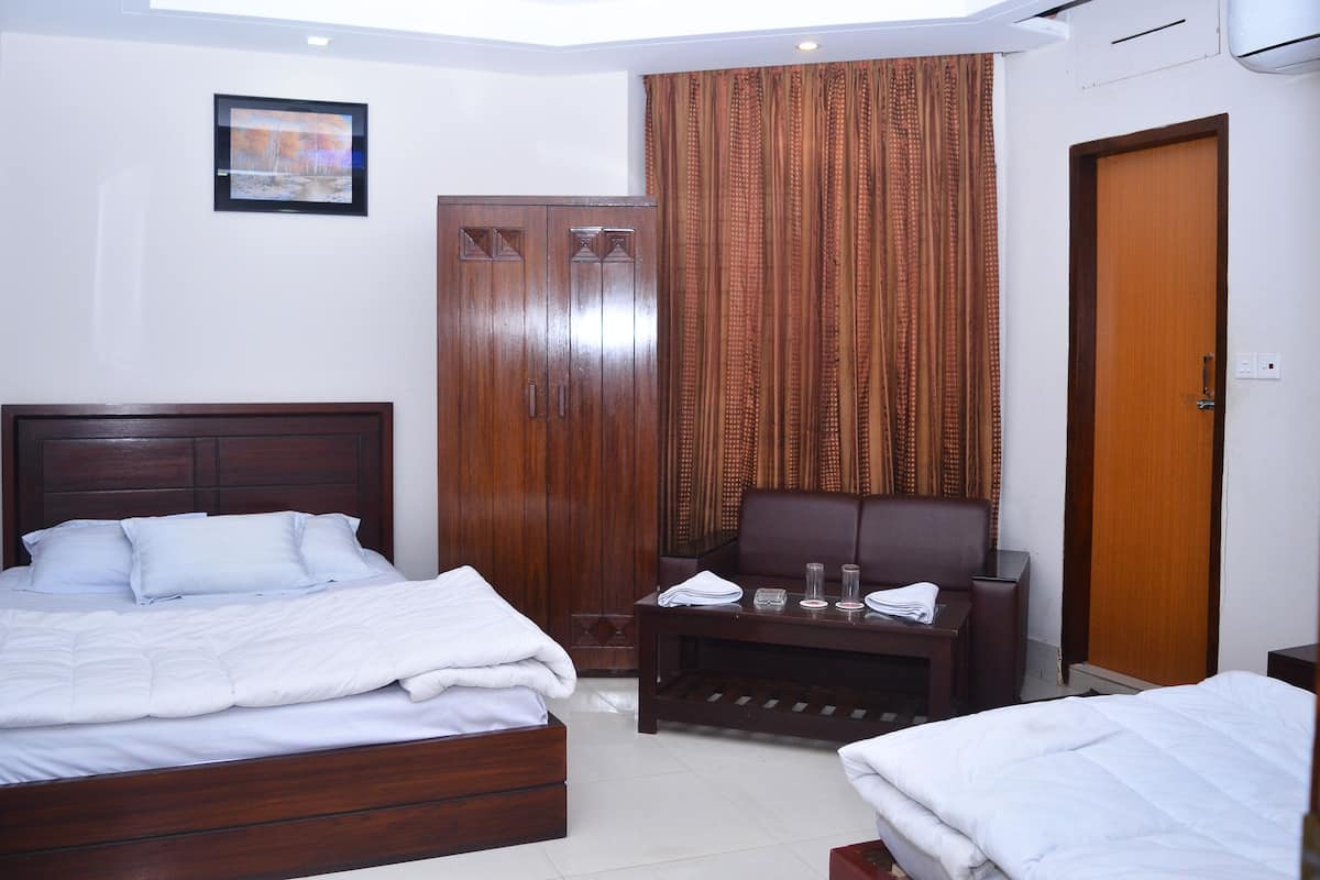 A hotel room with a wooden bed, a small table with a chair, a wardrobe, and a door.