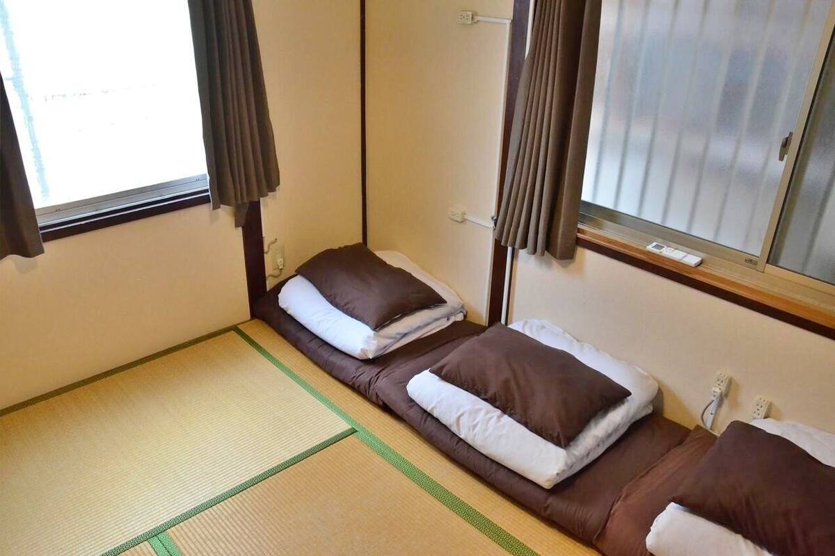 Una habitación pequeña con dos camas, una ventana con cortinas y suelo de tatami.