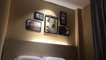 A hotel room with a bed, a headboard, and wall-mounted artwork including a picture of the Colosseum and a turtle.
