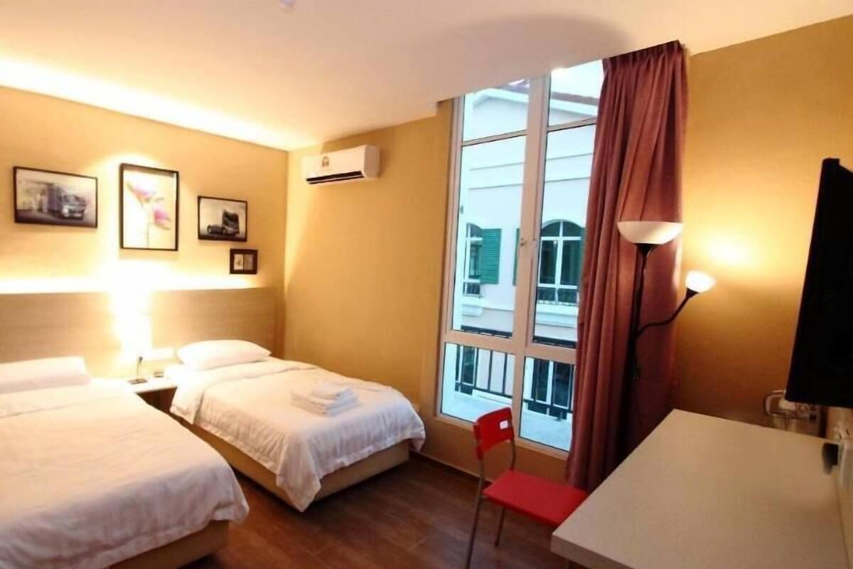 A hotel room with two beds, a desk, a chair, a TV, and a window with curtains.