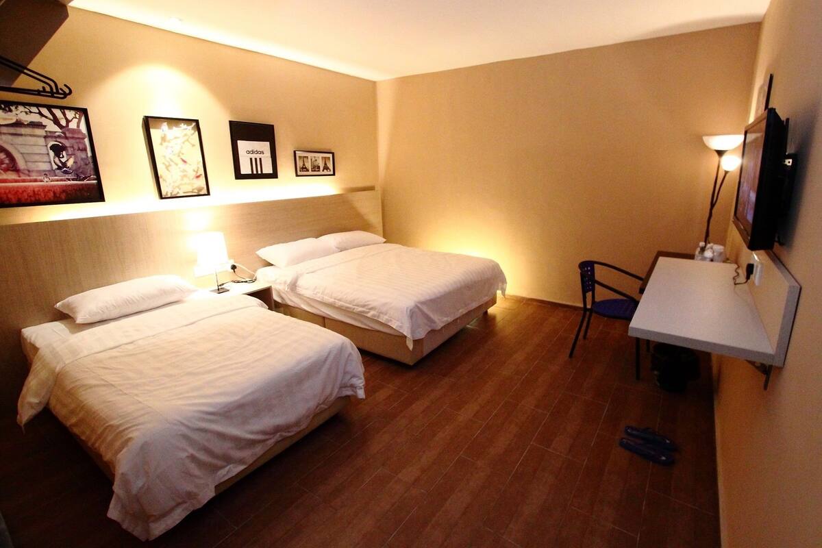 A hotel room with two beds, a desk, a chair, and a TV mounted on the wall.