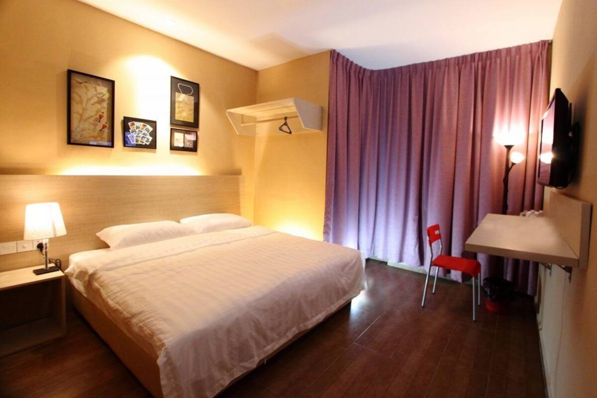 A hotel room with a bed, a desk, a chair, a TV, and a wall-mounted air conditioning unit.