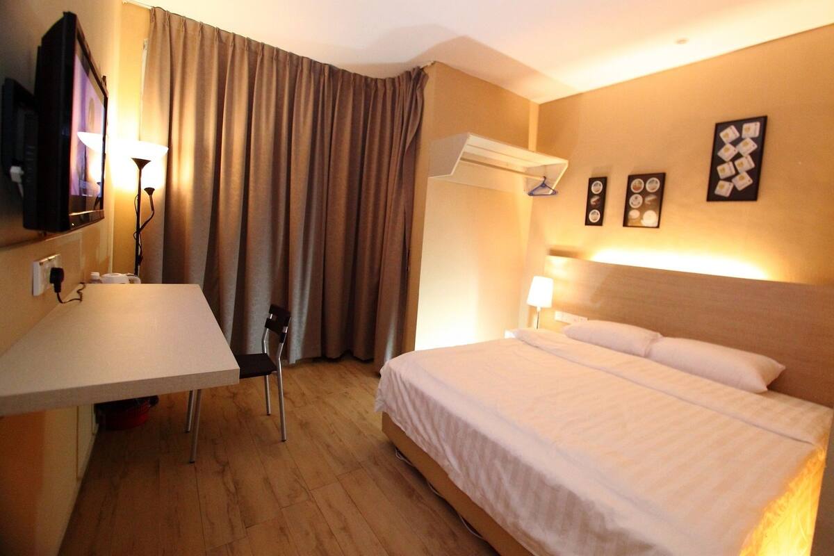 A hotel room with a bed, a desk, a chair, a TV, and a window with curtains.