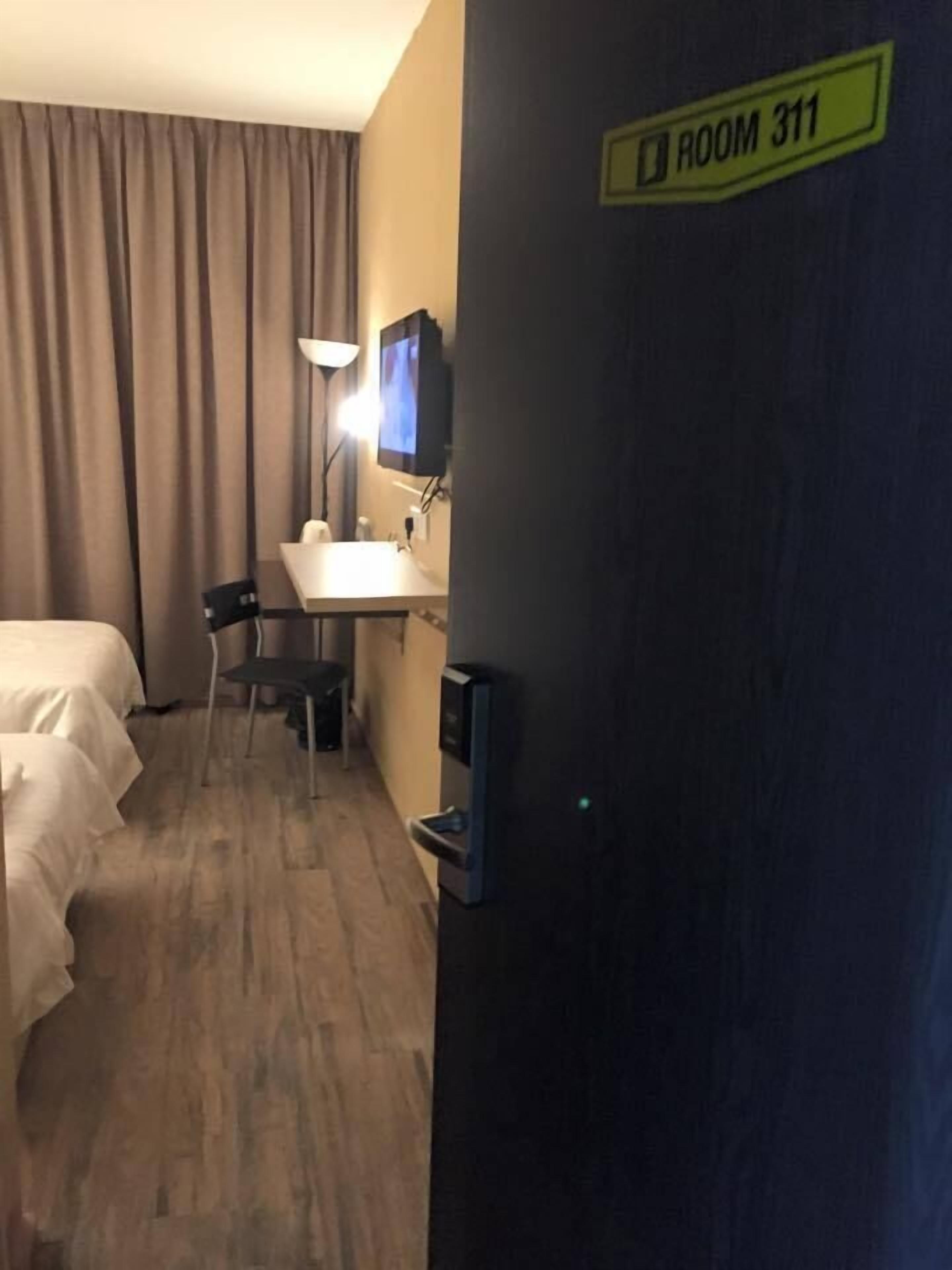 Une chambre d’hôtel équipée d’un lit, d’un bureau, d’une chaise, d’une télévision et d’une pancarte indiquant « Chambre 311 ».