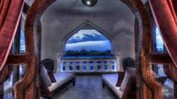 A room with a gothic arch window, two wooden benches, and a view of the sky and trees.