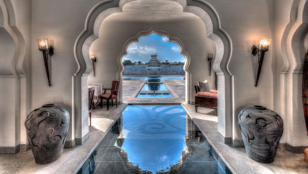 A pool area with a view of a temple, surrounded by arches and stone vases.