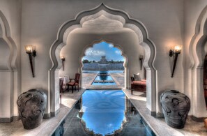 A pool area with a view of a temple, surrounded by arches and stone vases. - Evolve Back, Hampi (Hospet)
