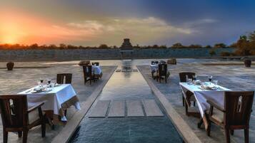 A dining area with tables set for two, a water feature in the center, and a stone wall in the background.