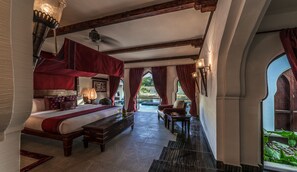 A bedroom with a canopy bed, a sitting area with a table and chairs, and a view of a garden through a window.