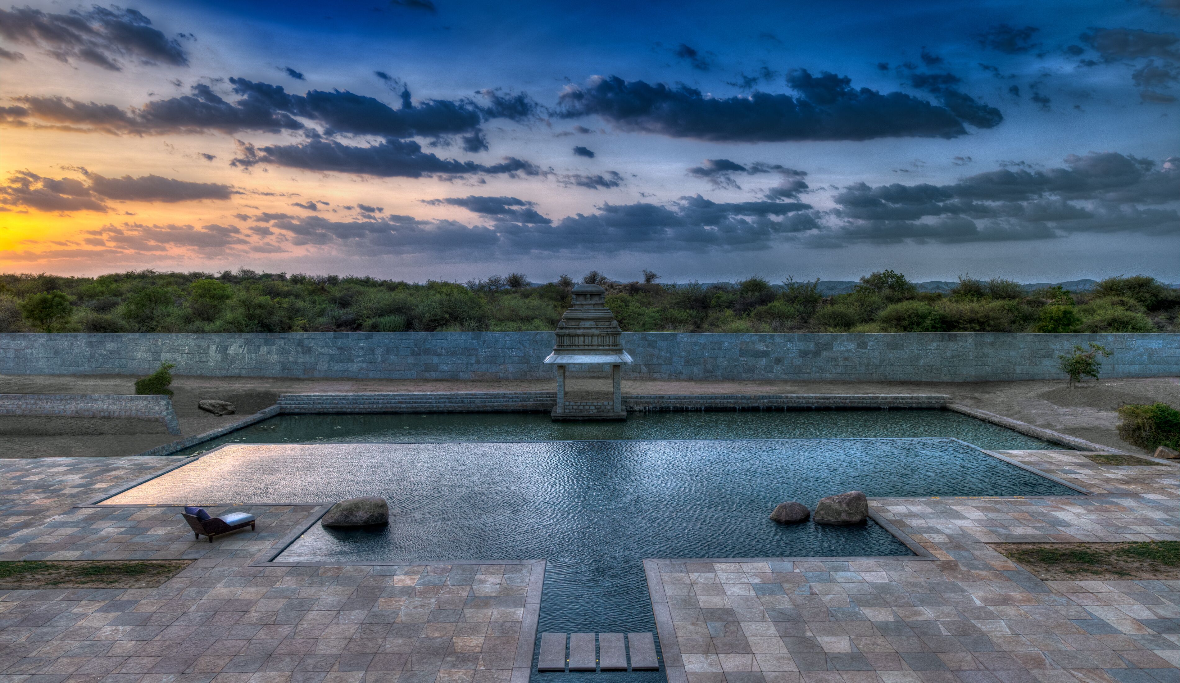 Una piscina con un farolillo de piedra, rodeada de muros de piedra y vista al cielo.
